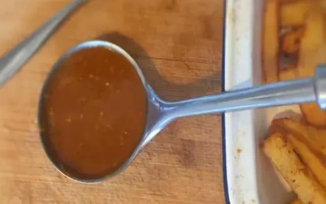 a ladle of curry sauce with a tray of chips