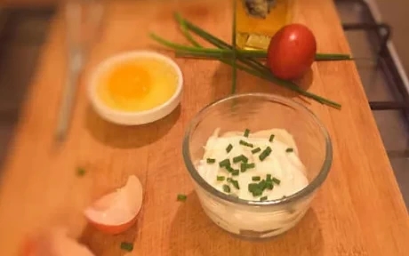 tub of mayonnaise with egg, oil and chives on a chopping board