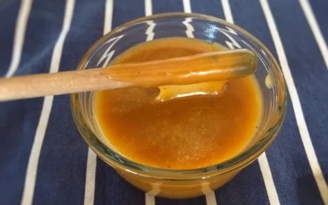 caramel sauce on a wooden spoon dripping into a pot of sauce